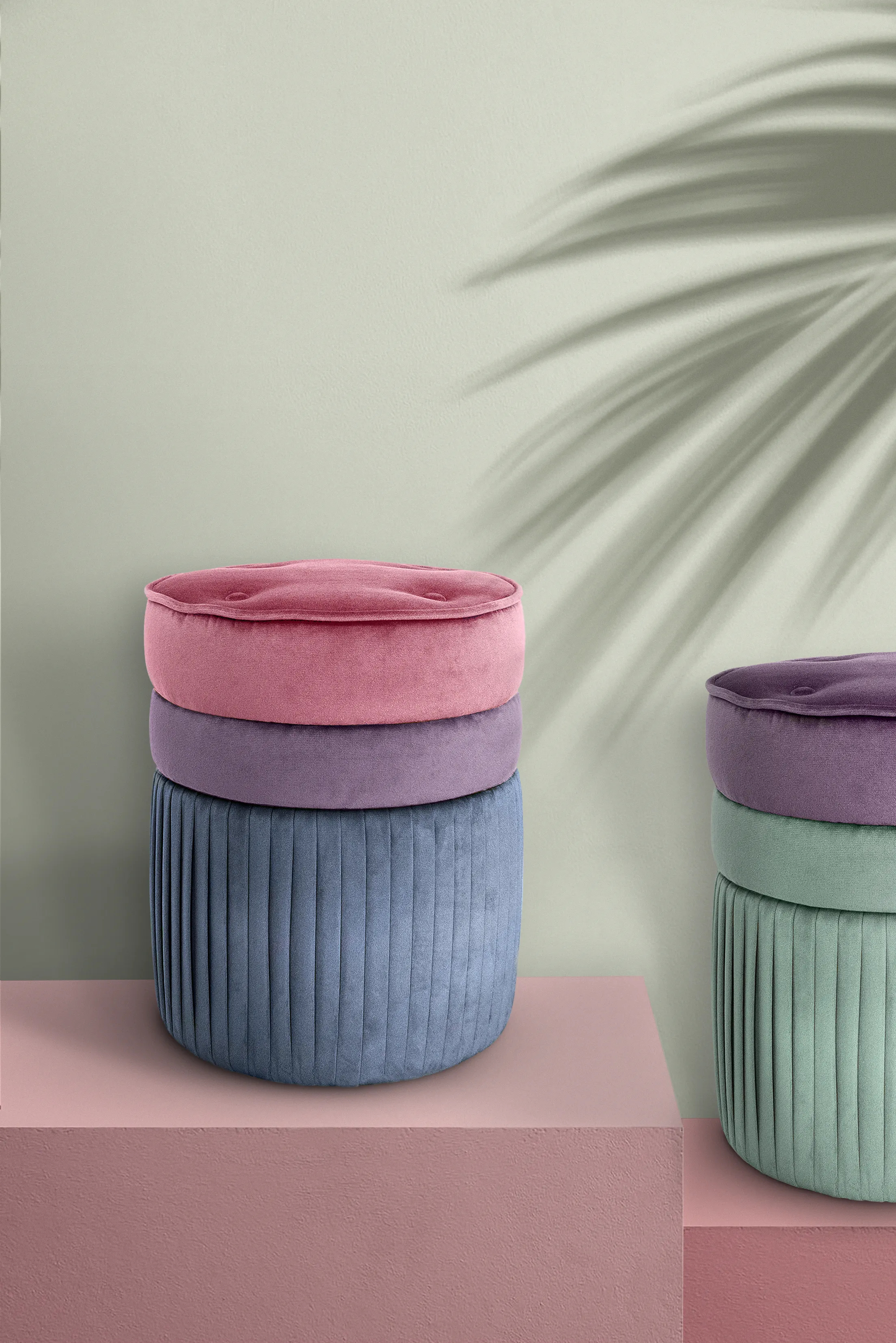 Contemporary Valencia Poufs with a smooth, rounded design in pastel-colored fabrics, placed in a sophisticated interior setting. A soft pink and grey background and a palm leaf shadow add sophistication and tropical flair.