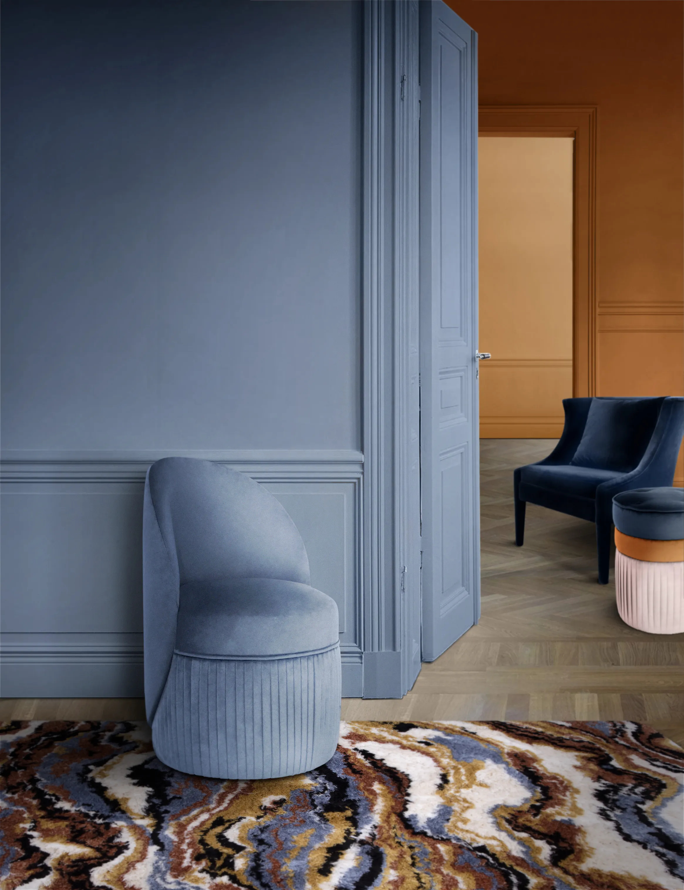 Venice Chair, upholstered with light blue fabric, navy velvet Athina Chair and three-toned fabric Valencia Pouf by KKbyKOKET. The furniture is settled in an inviting environment with matching blue tones and a fun patterned rug.